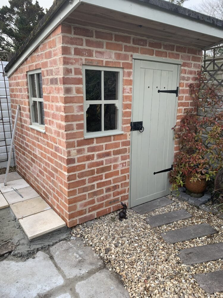 A timber framed outbuilding that has been over-clad using a tracking sheet and brick slips. The bricks are a reclaimed brick and the pointing is a mid grey colour