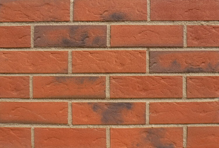 A brick panel with sandstone mortar in the joints. The bricks are a mid red colour with black accents. The brick slips are very accurate in dimensions with crisp, clean edges.