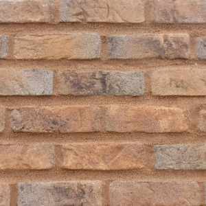 A panel of a batch of Matclad brick slips. The bricks are a multi coloured, sand coated hand made brick. The main colour of the brick is a mid orange with blue and black mottled throughout. The bricks are pointed with a light brown sandstone pointing mortar