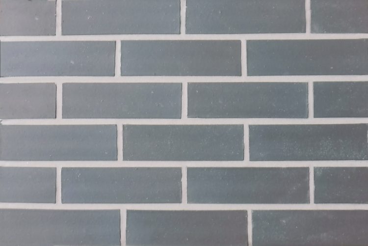 A black smooth brick slip panel. The edges of the brick are straight and square and the mortar is a mid grey